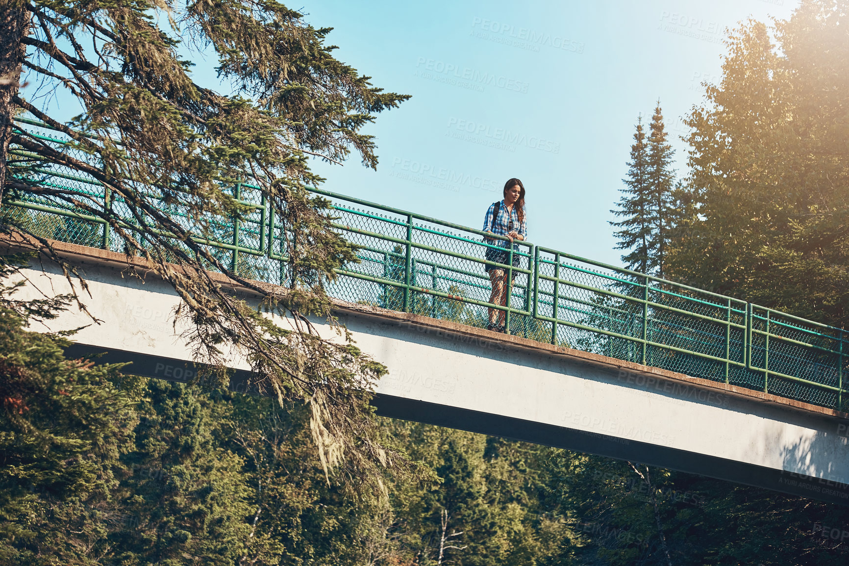 Buy stock photo Shot of an attractive young woman standing on a bridge surrounded by nature