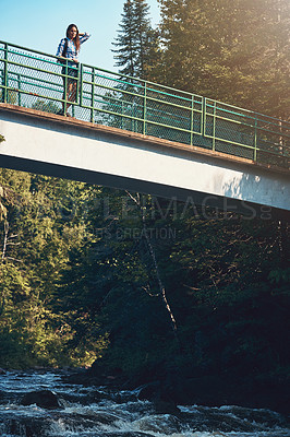 Buy stock photo Shot of an attractive young woman standing on a bridge surrounded by nature