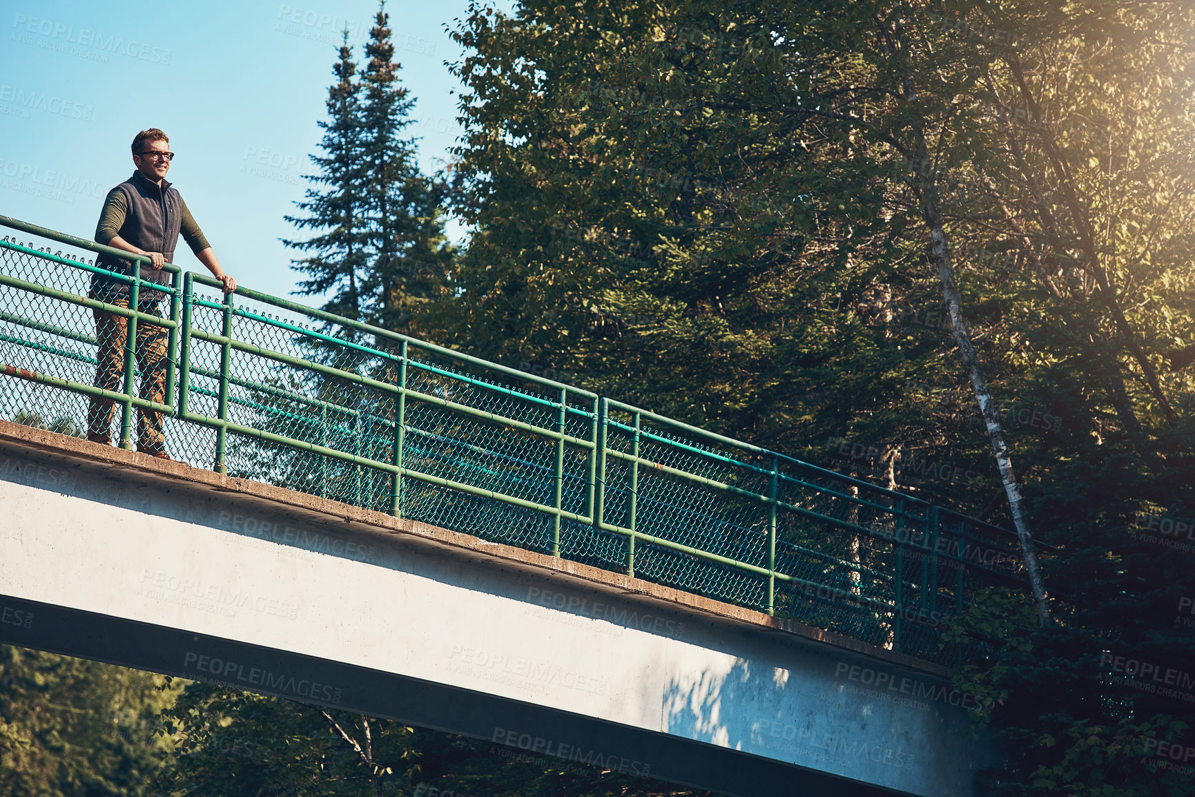 Buy stock photo Shot of a young man standing on a bridge surrounded by nature