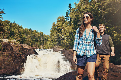 Buy stock photo Shot of a young couple walking next to a rocky river and waterfall