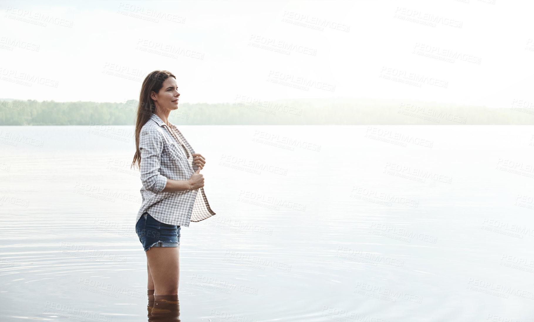 Buy stock photo Shot of an attractive young woman standing in a lake