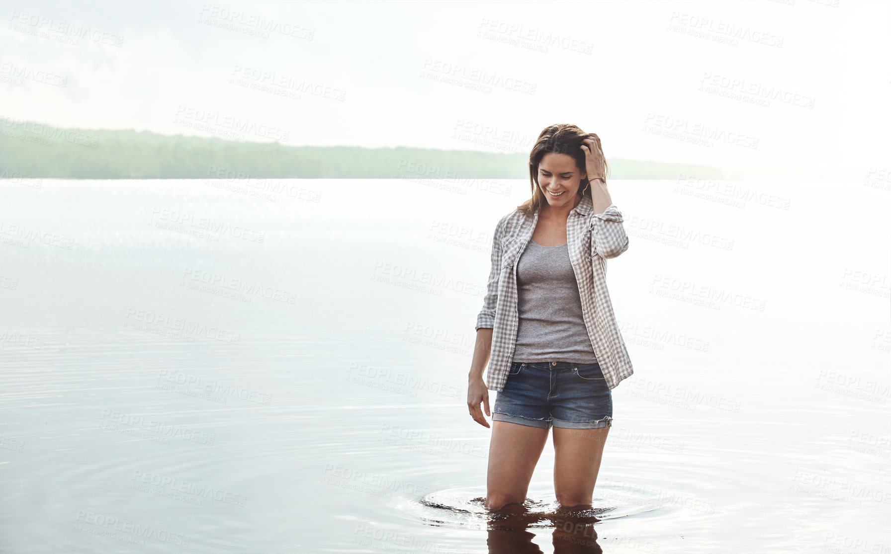 Buy stock photo Shot of an attractive young woman standing in a lake