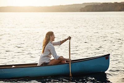 Buy stock photo Shot of a beautiful young woman rowing a boat out on the lake