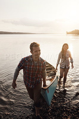 Buy stock photo Sunset, lake and couple with boat by water for adventure, summer and support. Happy man, woman and sunshine or teamwork help for travel, freedom and peace in nature and canoe for wellness 