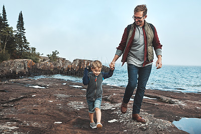 Buy stock photo Shot of a cheerful father and son holding hands while walking next to the ocean outside during the day