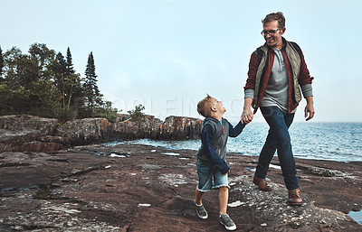Buy stock photo Shot of a cheerful father and son holding hands while walking next to the ocean outside during the day