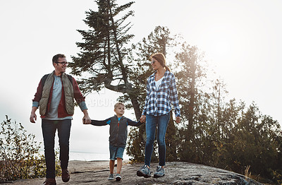 Buy stock photo Shot of a cheerful young family standing on top of a hill while holding hands outside during the day