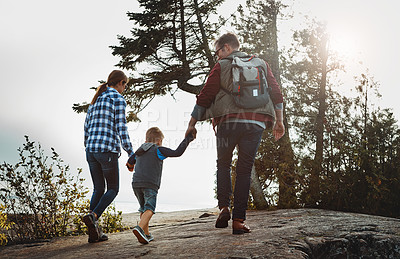 Buy stock photo Rearview shot of a cheerful young family holding hands and walking together up a hill outside during the day