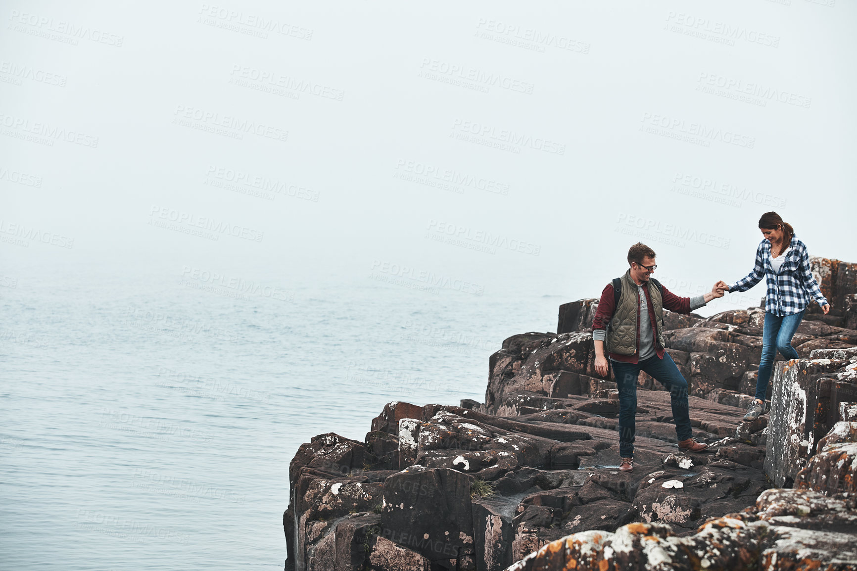 Buy stock photo Shot of a handsome young man assisting his girlfriend while out climbing a mountain