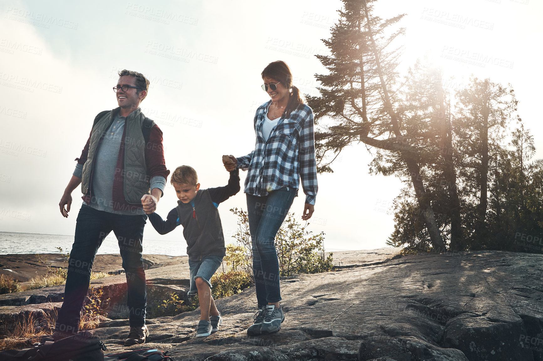 Buy stock photo Shot of a cheerful young family holding hands and walking together down a hill outside during the day