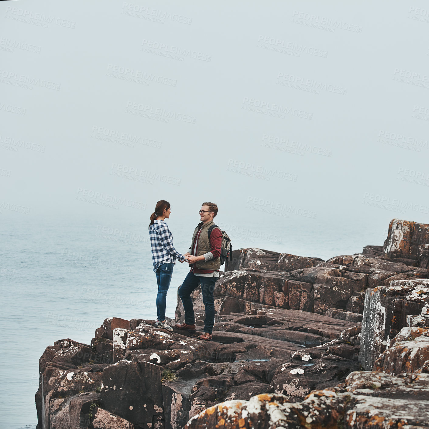 Buy stock photo Shot of a loving young couple standing hand in hand on a mountaintop