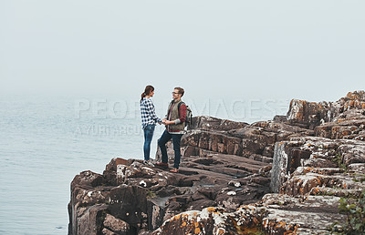 Buy stock photo Shot of a loving young couple standing hand in hand on a mountaintop