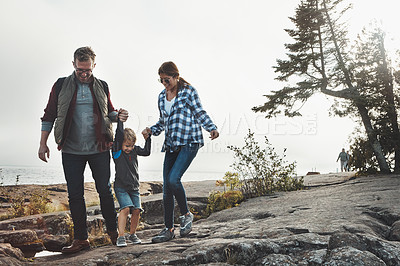 Buy stock photo Shot of a cheerful young family holding hands and walking together down a hill outside during the day