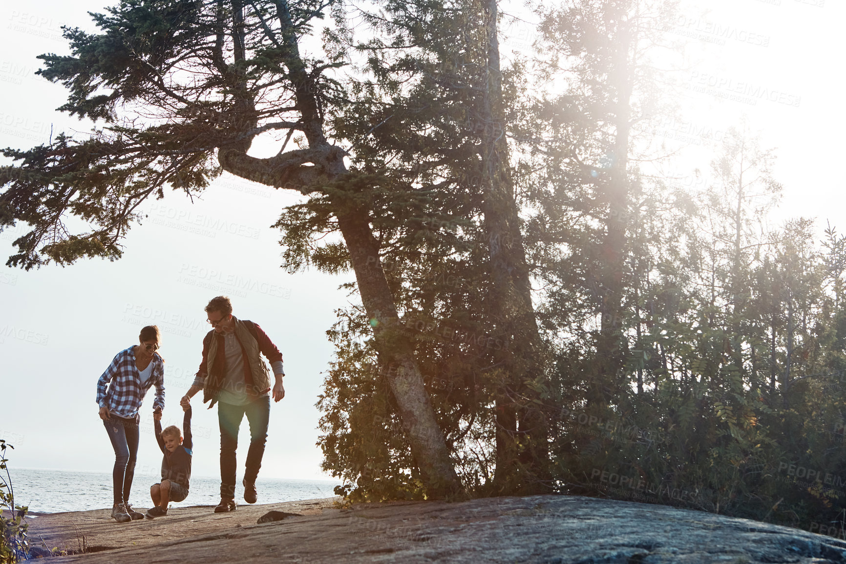 Buy stock photo Wide shot of a cheerful young family holding hands and walking together down a hill outside during the day