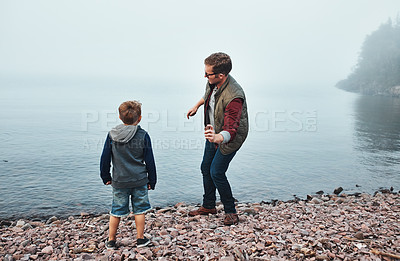 Buy stock photo Rearview shot of a cheerful father and son throwing flat stones into a lake while standing next to the water