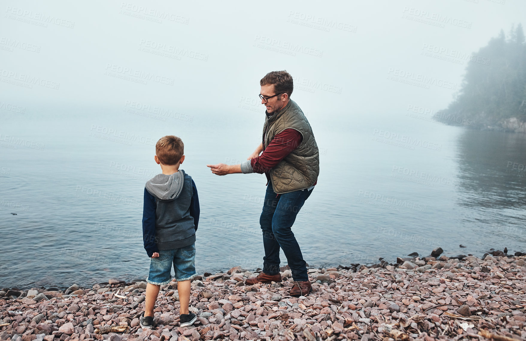 Buy stock photo Rearview shot of a cheerful father and son throwing flat stones into a lake while standing next to the water
