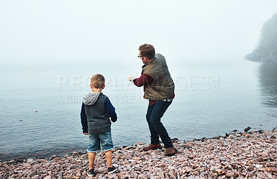 Buy stock photo Rearview shot of a cheerful father and son throwing flat stones into a lake while standing next to the water
