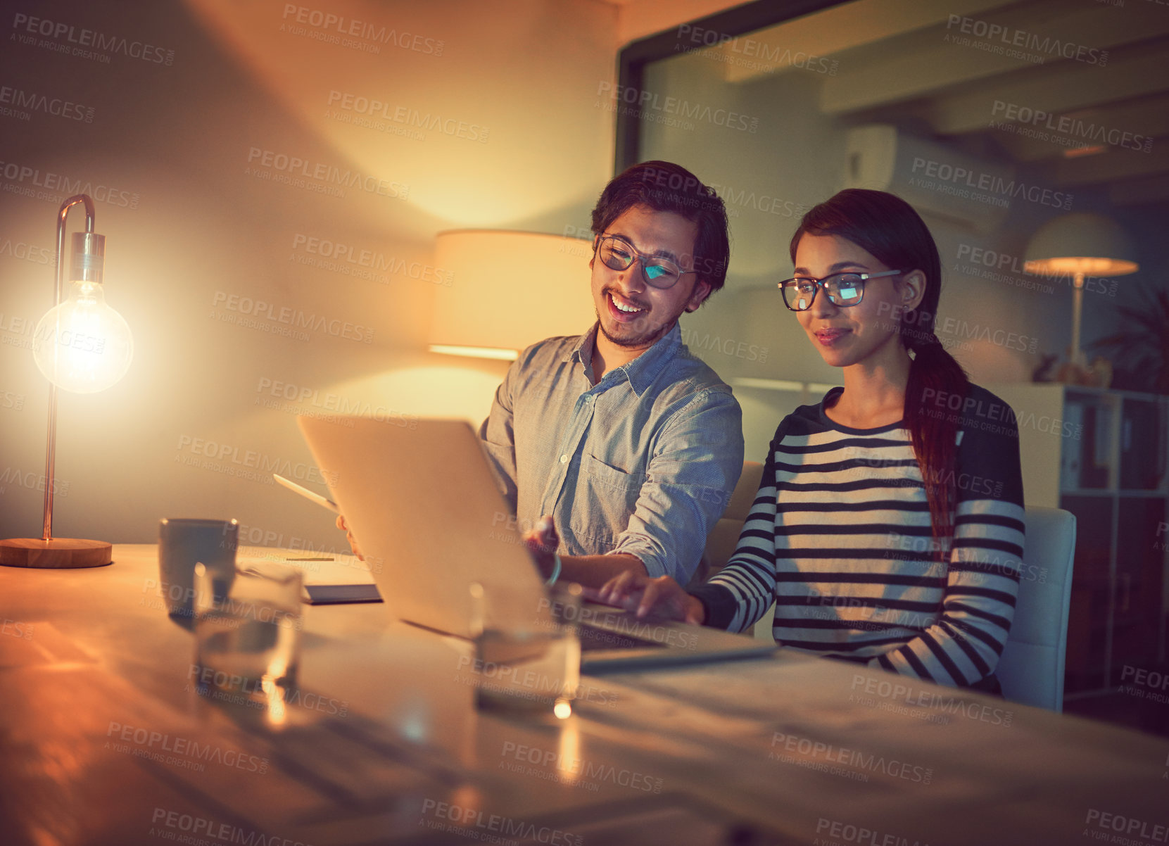Buy stock photo Shot of two young designers working late on a laptop in an office