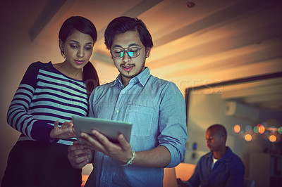 Buy stock photo Shot of two young designers working late on a digital tablet in an office
