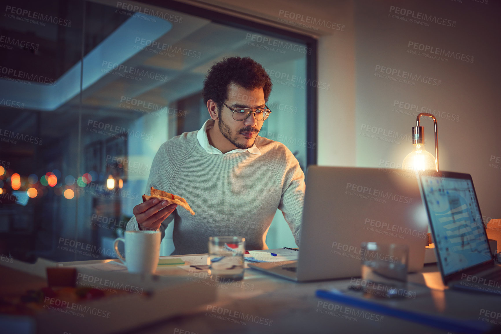 Buy stock photo Shot of a young designer eating pizza while working late in an office