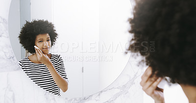 Buy stock photo Shot of a confident young woman wiping her face with a cleanser while looking into a mirror in the bathroom at home during the day