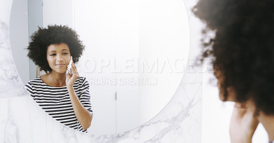 Buy stock photo Shot of a confident young woman wiping her face with a cleanser while looking into a mirror in the bathroom at home during the day