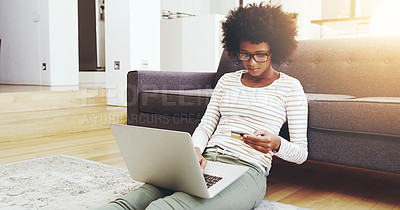Buy stock photo Shot of a focused young woman seated on the floor while doing online shopping on her computer in the living room at home