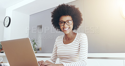 Buy stock photo Portrait of a cheerful young woman typing and working on a laptop while being seated next to a table at home