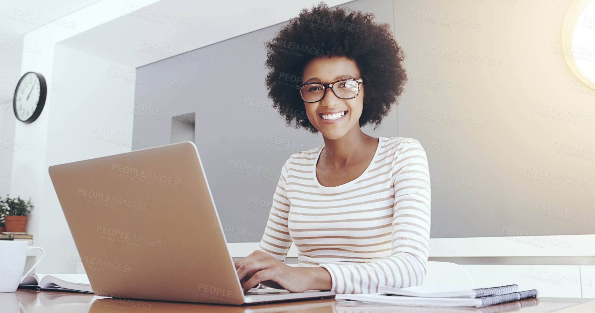 Buy stock photo Portrait of a cheerful young woman typing and working on a laptop while being seated next to a table at home