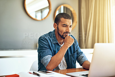Buy stock photo Shot of a focused young man working on his laptop while contemplating behind a table at home