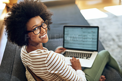 Buy stock photo Portrait of a cheerful young woman working on her laptop while being seated comfortably on a couch at home