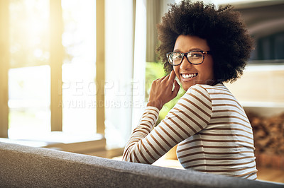 Buy stock photo Portrait of a cheerful young woman seated comfortably on a couch at home during the day