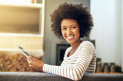 Buy stock photo Portrait of a cheerful young woman browsing on her digital tablet while being seated comfortably on a couch at home