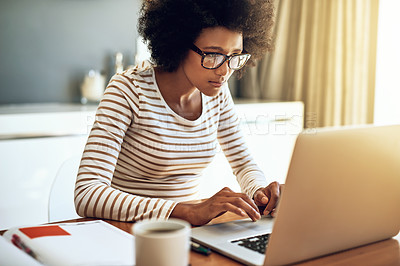 Buy stock photo Shot of a confident young woman working on her laptop while drinking a cup of coffee at home during the day