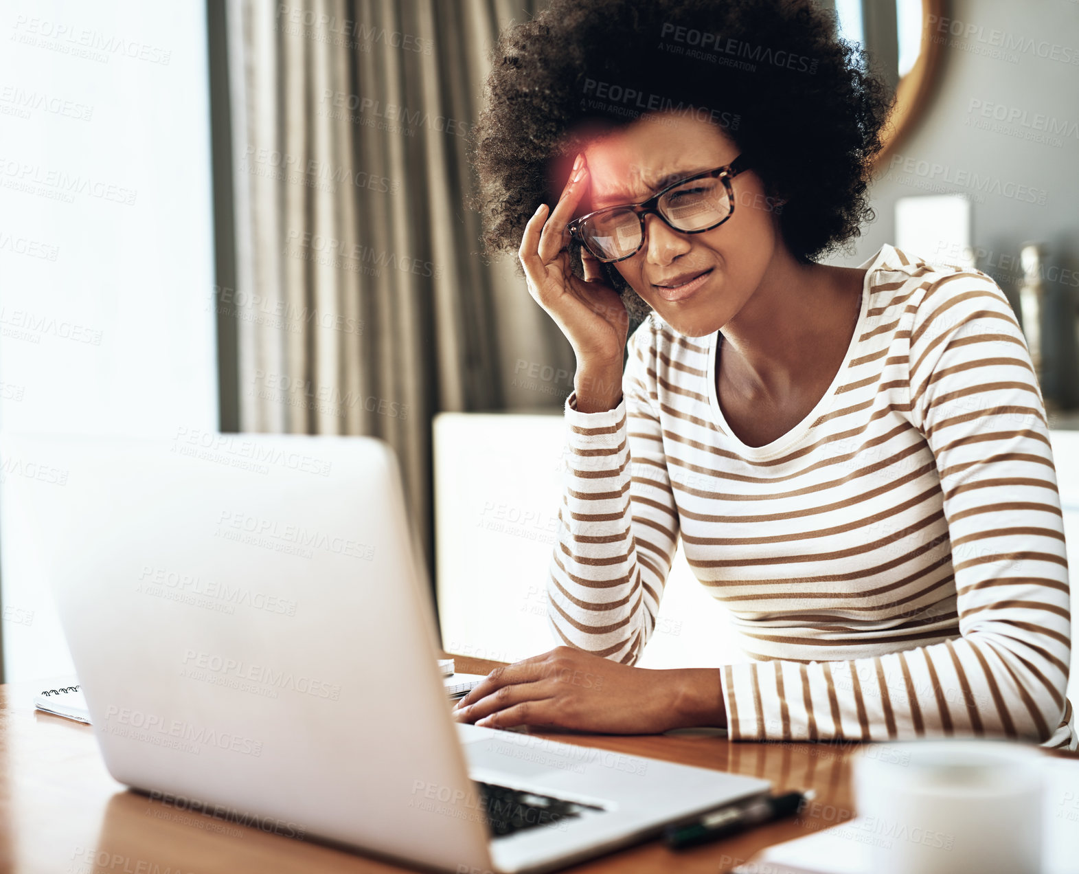 Buy stock photo Shot of a stressed young woman working on her laptop while holding the side of her head in discomfort due to pain