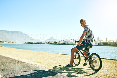 Buy stock photo Full length portrait of a young boy riding his bike alongside a lagoon