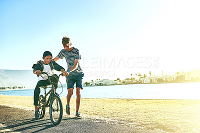 Buy stock photo Outdoor, ride and siblings with bicycle for learning, paddle or coordination with balance by space. Lagoon, children or boys with bike for speed, moving or teenage brother with assistance for support
