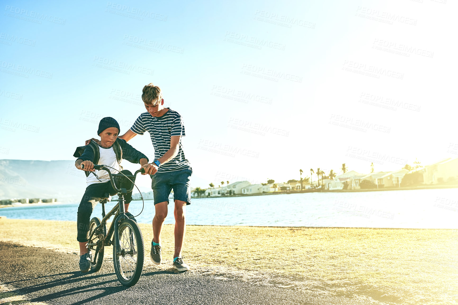 Buy stock photo Outdoor, ride and siblings with bicycle for learning, paddle or coordination with balance by space. Lagoon, children or boys with bike for speed, moving or teenage brother with assistance for support