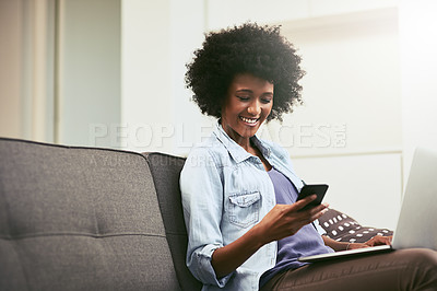 Buy stock photo Shot of a young woman using a laptop and mobile phone on the sofa at home