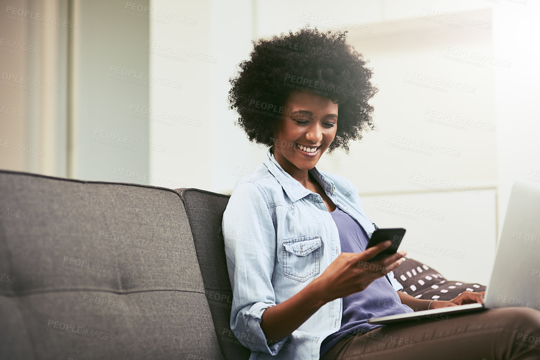 Buy stock photo African woman, phone and laptop on couch in house for internet, email and mobile app with smile. Technology, chat and remote work as social media manager for company, agency or business in home