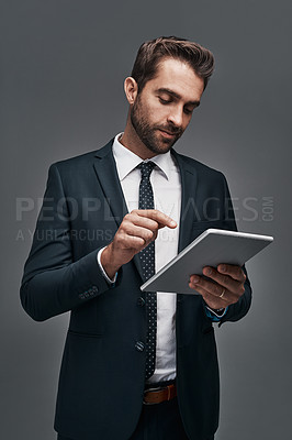 Buy stock photo Studio shot of a handsome young businessman using a digital tablet against a grey background