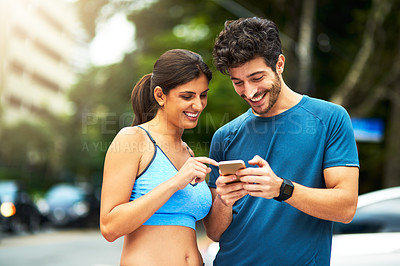 Buy stock photo Shot of a sporty young couple using a cellphone while exercising outdoors
