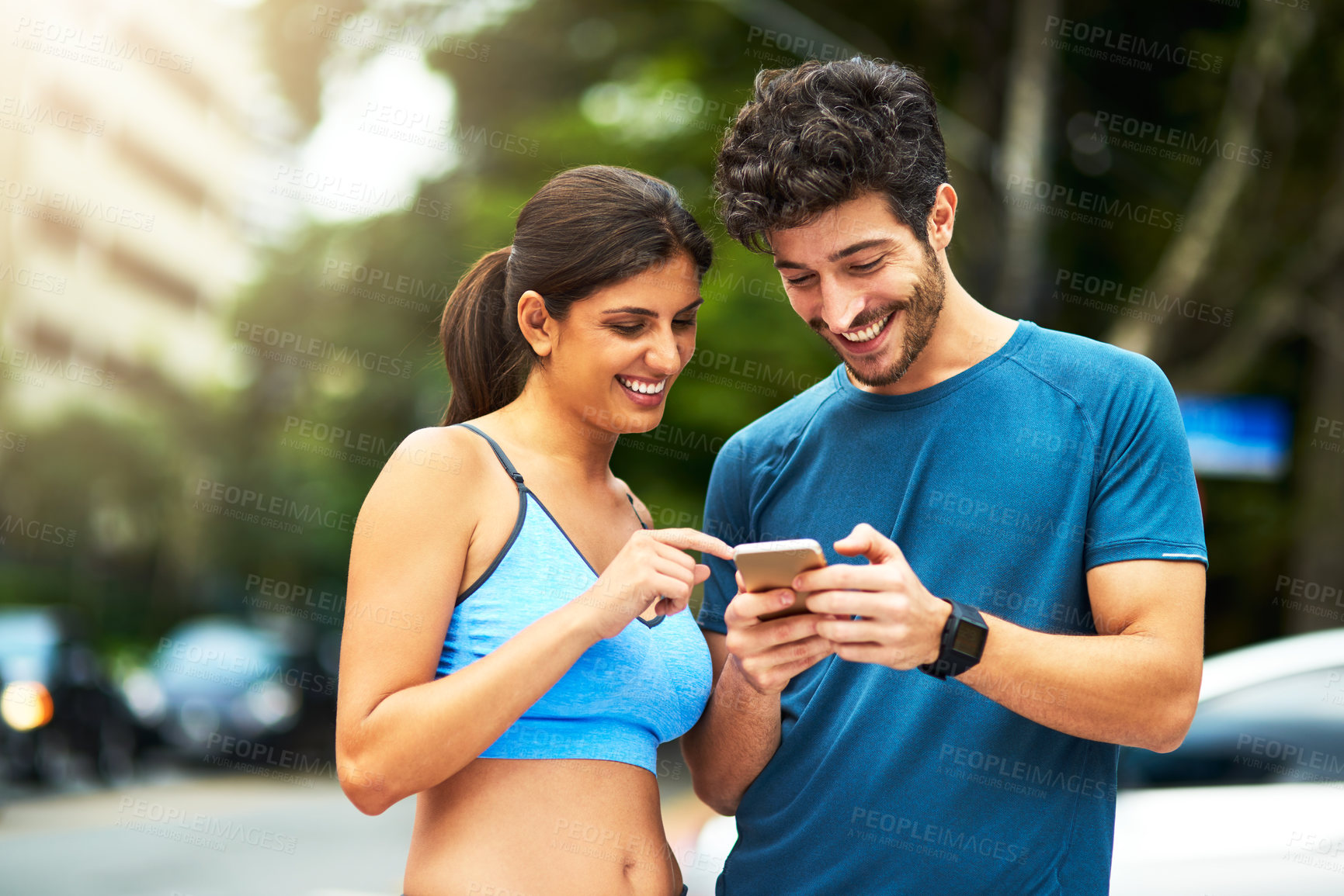 Buy stock photo Shot of a sporty young couple using a cellphone while exercising outdoors