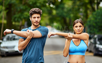 Buy stock photo Portrait of a sporty young couple stretching while exercising together outdoors