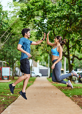 Buy stock photo Shot of a sporty young couple high fiving in mid-air while exercising outdoors