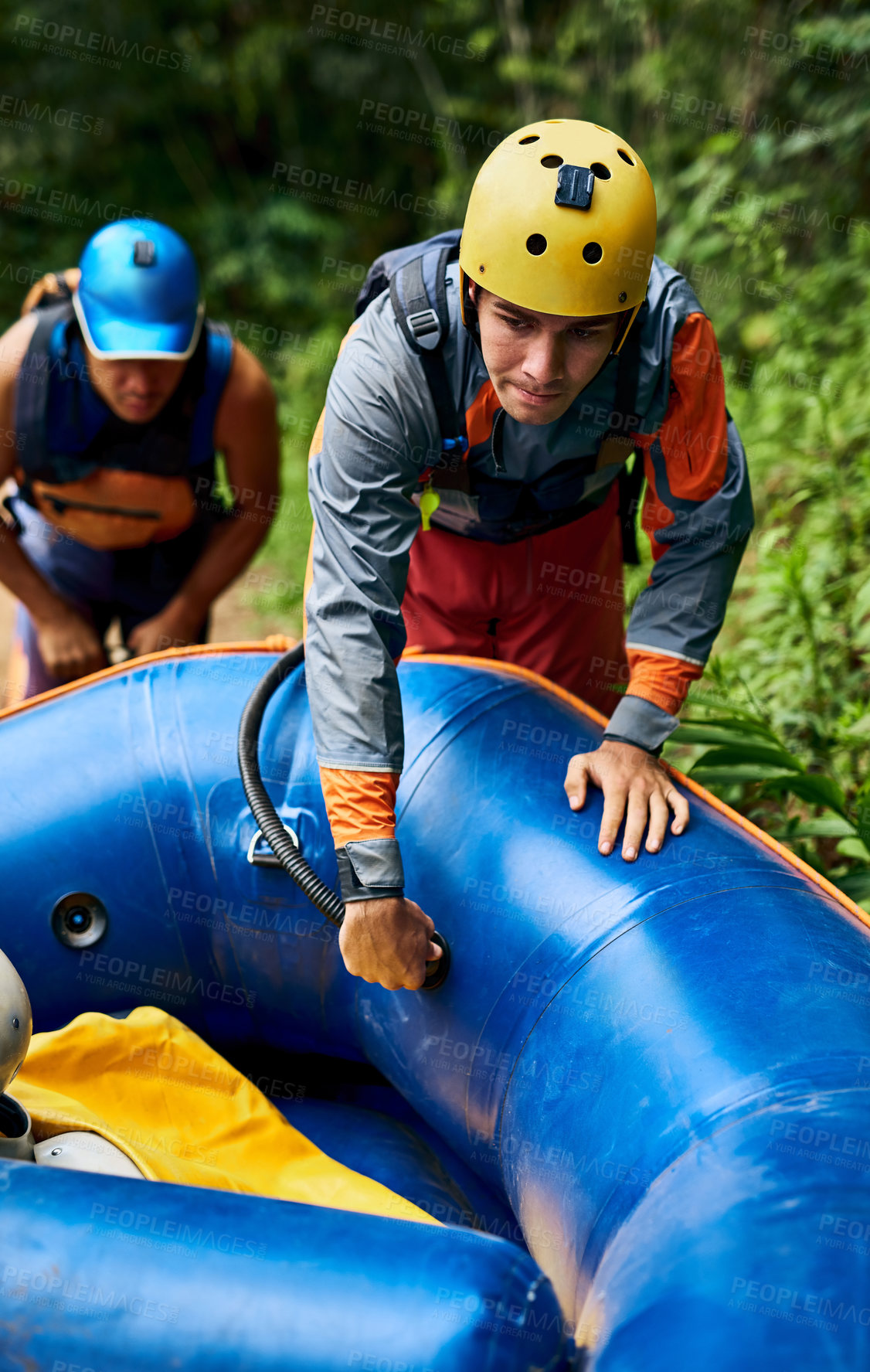 Buy stock photo Shot of a determined young man wearing protective gear while dragging a rubber boat outside during the day