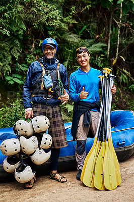 Buy stock photo Portrait of two cheerful men standing together next to a rubber boat while holding river rafting equipment outside during the day