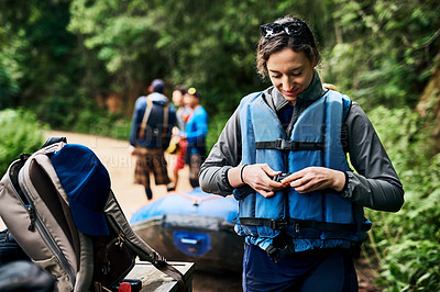 Buy stock photo Shot of a cheerful young woman putting on a life jacket to go river rafting outside during the day