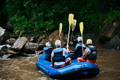 Buy stock photo Rearview shot of a group of unrecognizable people sitting in a rubber boat on a river while raising their paddles in the air outside during the day