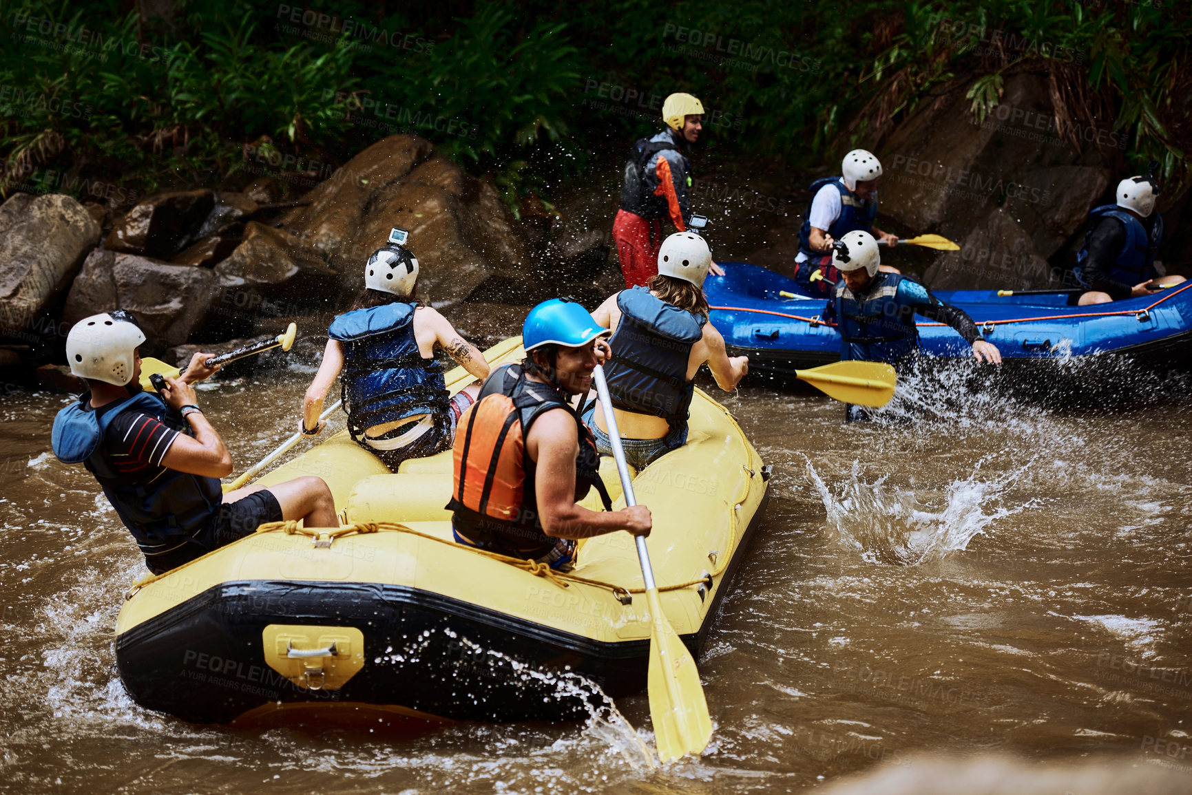 Buy stock photo Shot of a group of cheerful young people in a rubber boat paddling on a river outside during the day